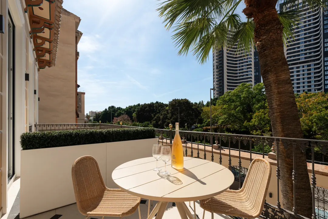 The sunny balcony of the Azuri residence, with a table and chairs overlooking gardens and the city of Málaga