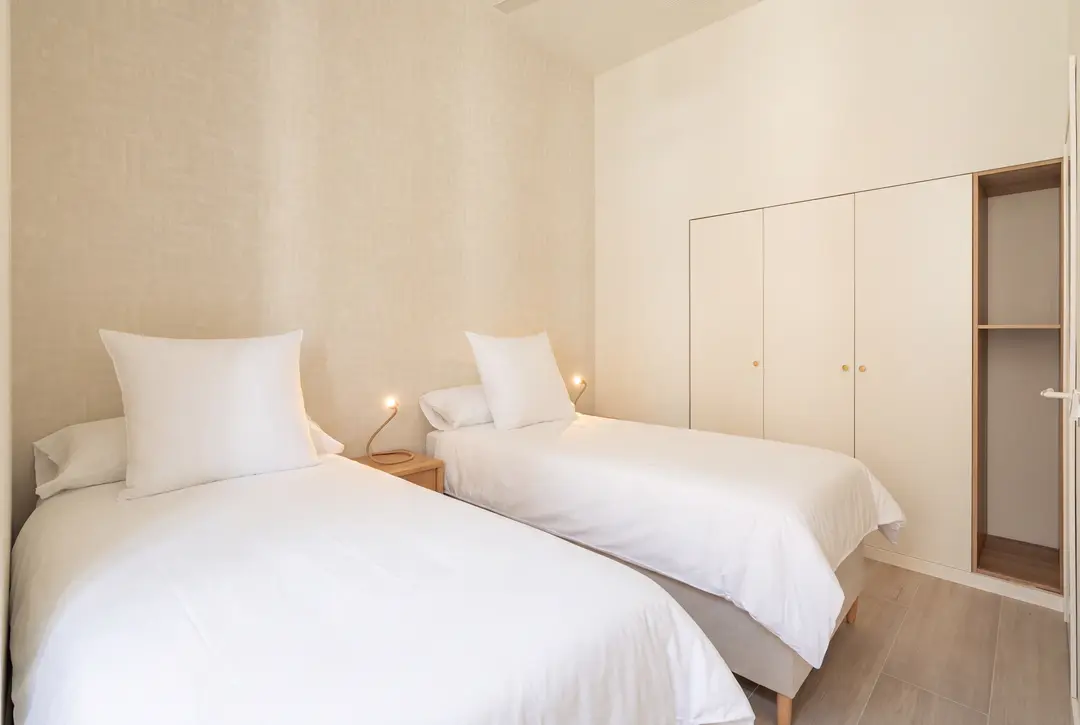 A twin bedroom in the Azuri residence with two single beds, white quilted bedspreads, and built-in wardrobes in neutral tones