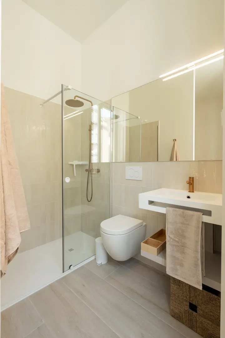 The bathroom in the Azuri residence, with a walk-in shower, wall-hung toilet, and a modern white basin with bronze fittings