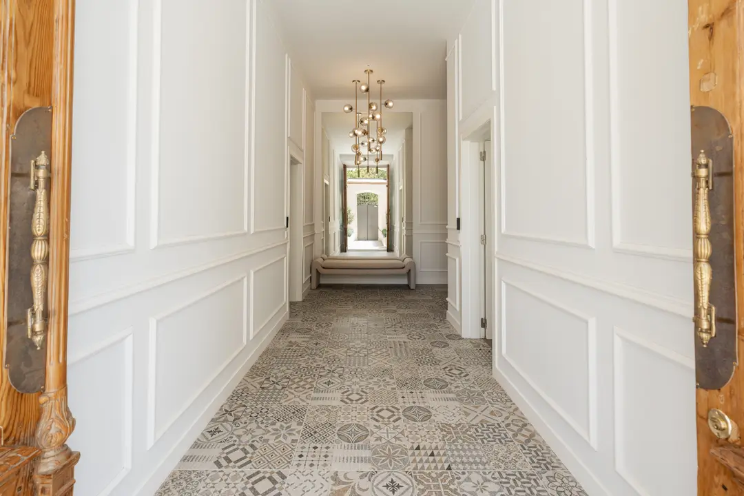 The long entrance hall at Palacete 10, seen from the open front doors, with patterned tiles, white panelled walls and a bench at the far end