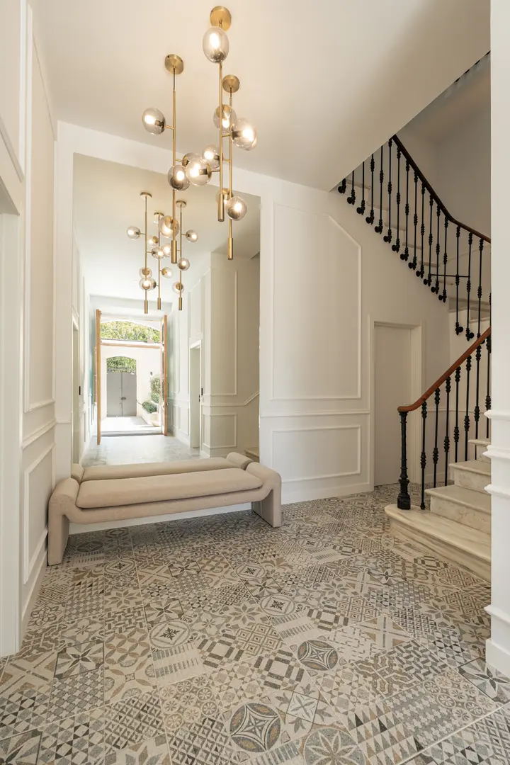 The entrance hall of Palacete 10, with patterned floor tiles, a marble staircase, and modern brass and glass pendant lights