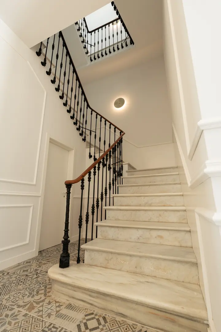 The original 1908 marble staircase at Palacete 10, with its wrought-iron banister and patterned floor tiles
