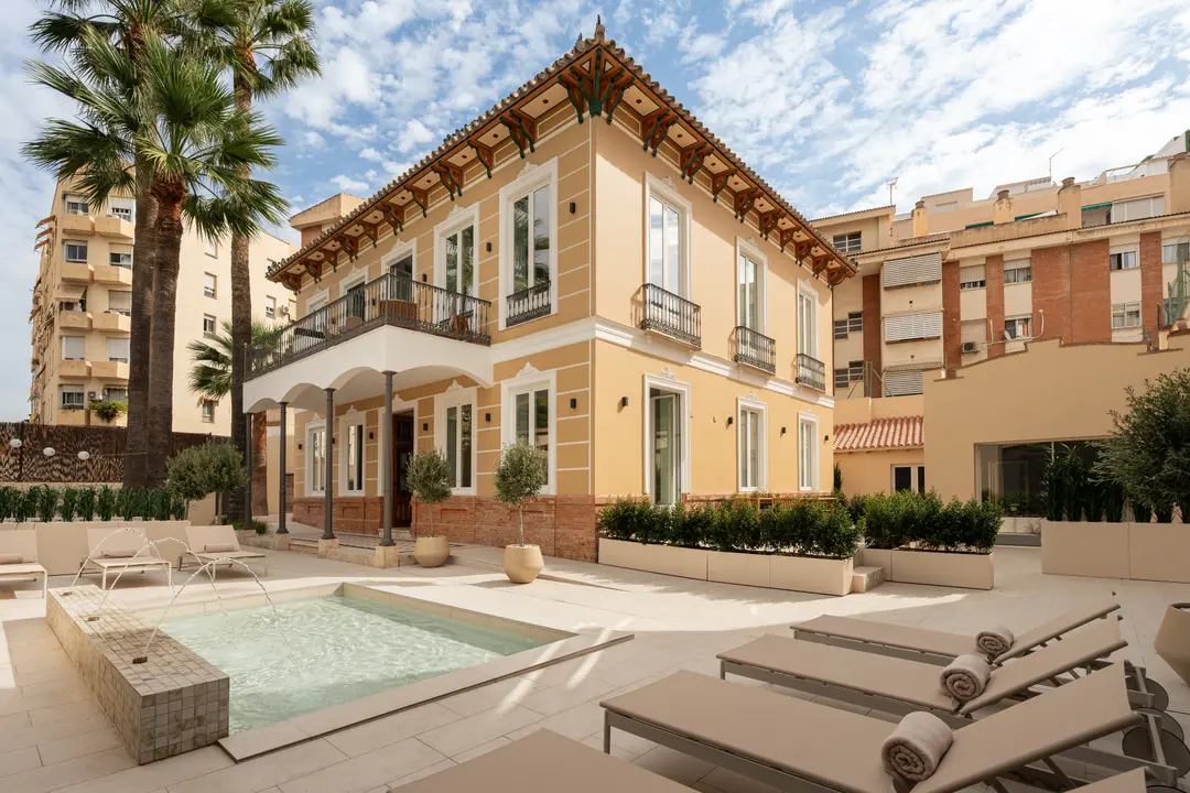 The restored yellow facade of Palacete 10, seen from the courtyard with its pond, sun loungers, and palm trees