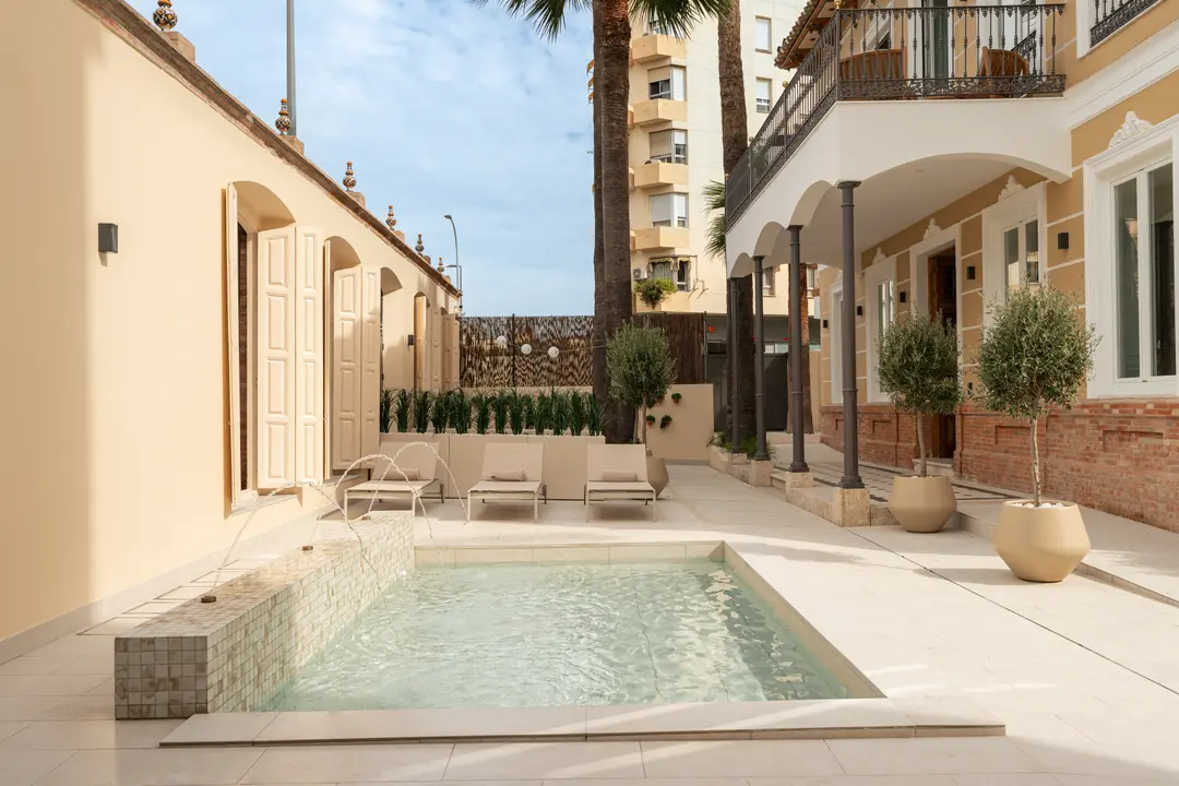 The shared courtyard at Palacete 10 with its tiled pond, fountains, sun loungers, and potted olive trees under a blue sky
