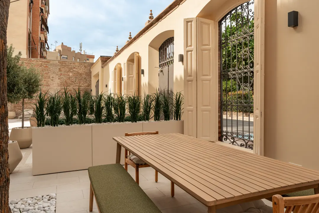 A wooden dining table with a green bench on the stone patio of the shared courtyard at Palacete 10