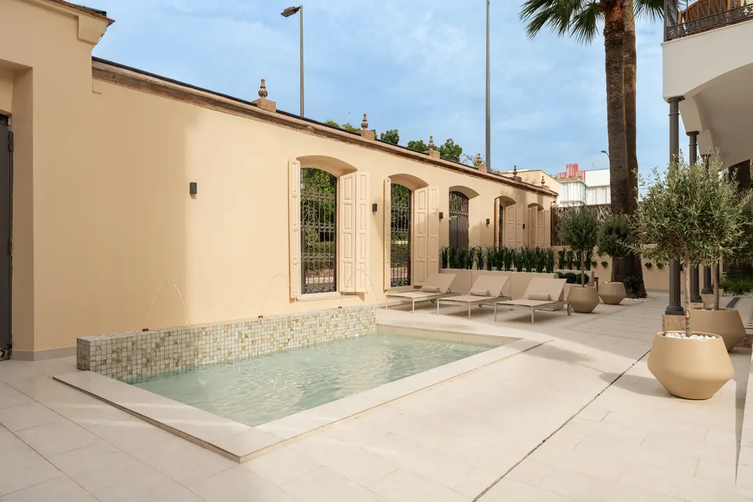 The shared courtyard with its tiled pond and fountains, sun loungers, and potted olive trees next to a restored facade