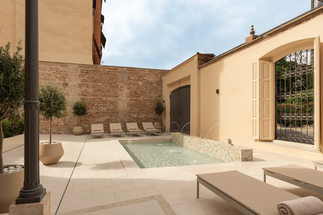 The shared courtyard at Palacete 10 with its stone patio, pond with fountains, and sun loungers beside an old brick wall