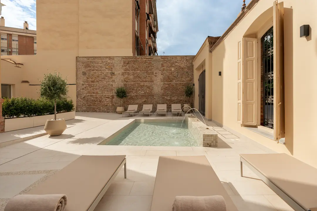 The sunny shared courtyard at Palacete 10, with a stone-paved terrace, pond, fountain, and beige sun loungers