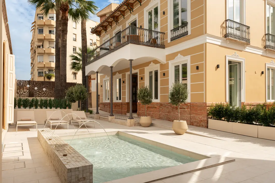 The restored yellow facade of Palacete 10 seen from the courtyard, with its tiled pond, fountains, and sun loungers
