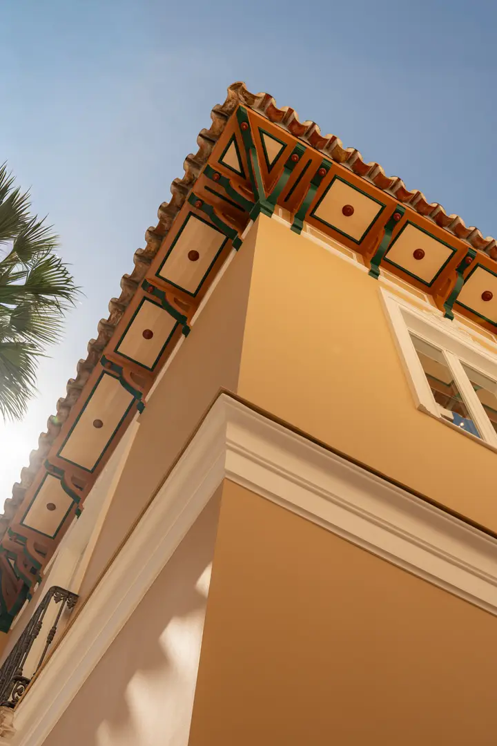 Low-angle view of the corner of the ochre facade, showing the decorated wooden eaves under a tiled roof against a blue sky