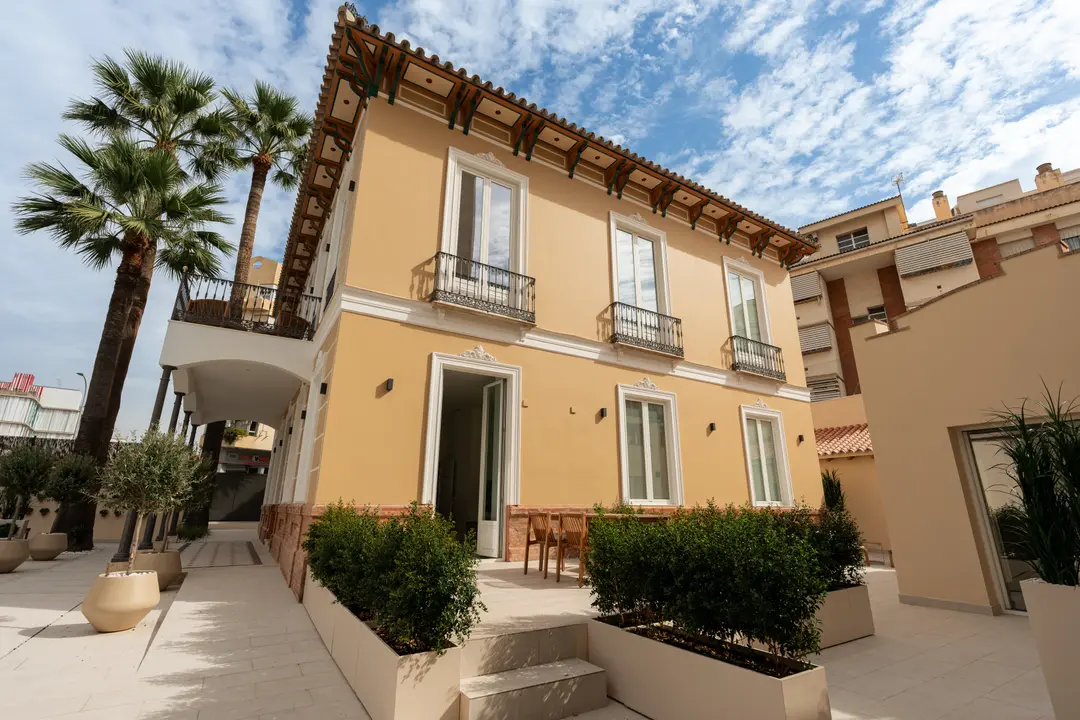 The restored yellow facade of Palacete 10 seen from the courtyard, with its palm trees, planters, and balconies