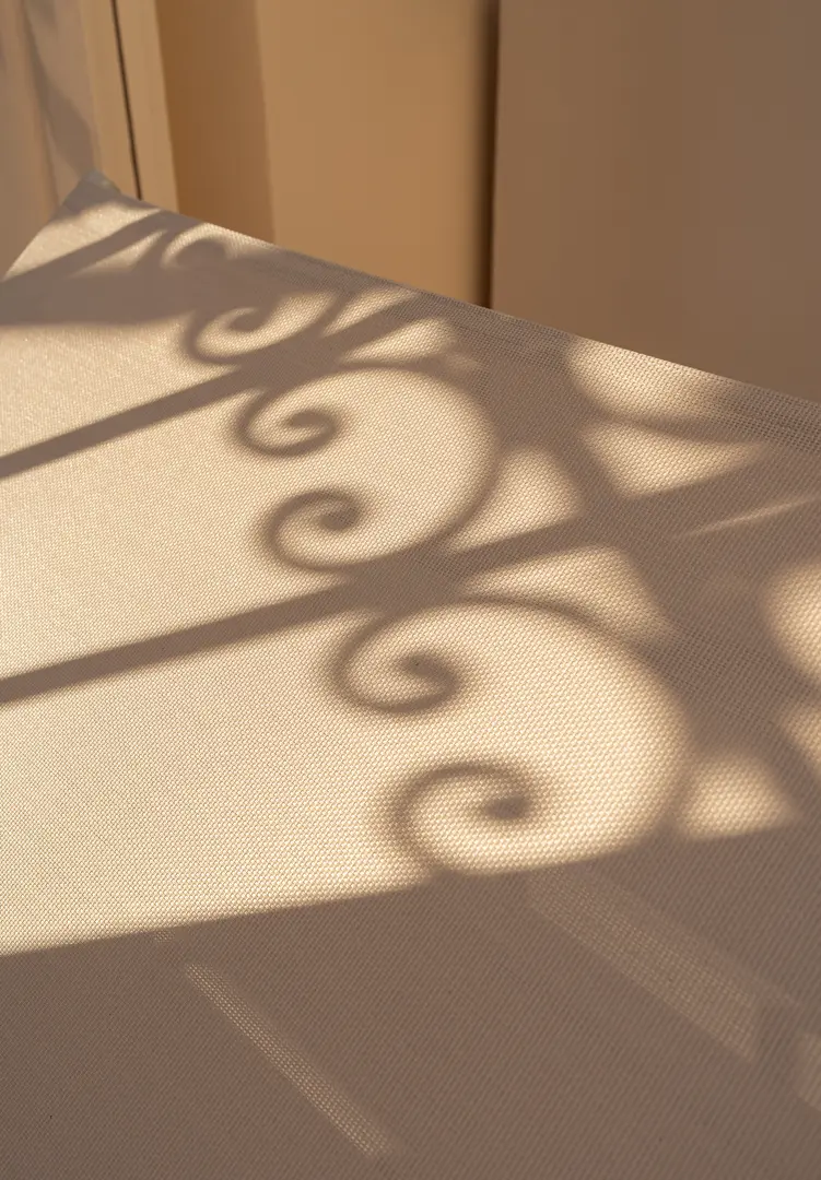 Close-up of the shadow of a wrought-iron balcony railing cast by warm sunlight onto a textured beige surface