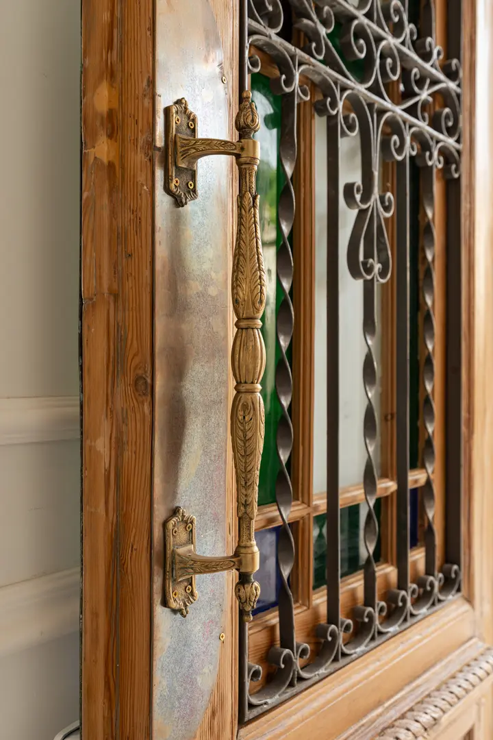 Close-up of the ornate brass handle on the restored wooden entrance door with its wrought-iron grille at Palacete 10