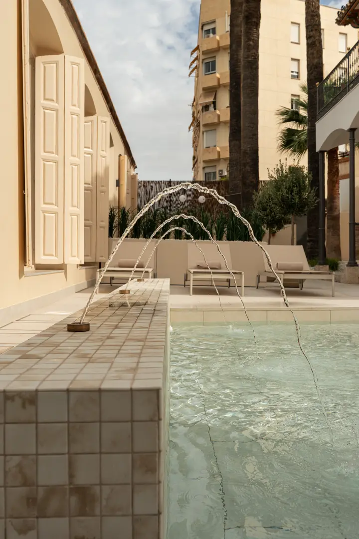 Water jets arch into the tiled pond in the courtyard, with sun loungers on the terrace next to the villa