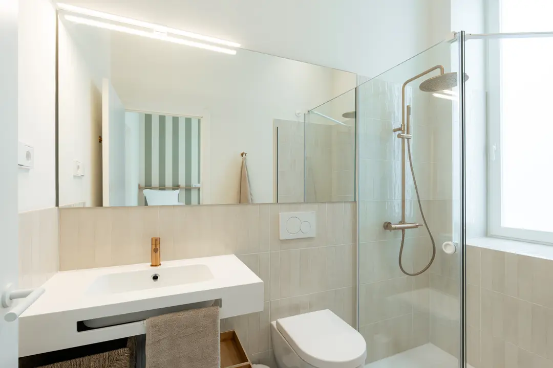 Bathroom in the Oliva residence with a white sink, bronze tap, and a walk-in rain shower with glass screen