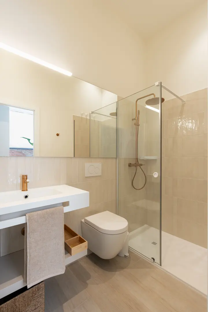 Bathroom in the Oliva residence with a walk-in shower, wall-hung toilet, and a white vanity with copper-coloured fittings
