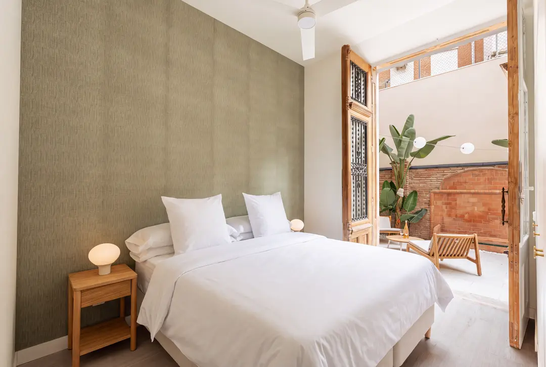 Bedroom in the Oliva residence with a double bed, sage green feature wall, and large antique wooden doors open to a private patio