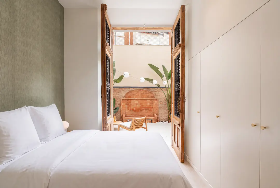 Bedroom in the Oliva residence with a textured green wall and tall antique doors opening onto a private patio with plants