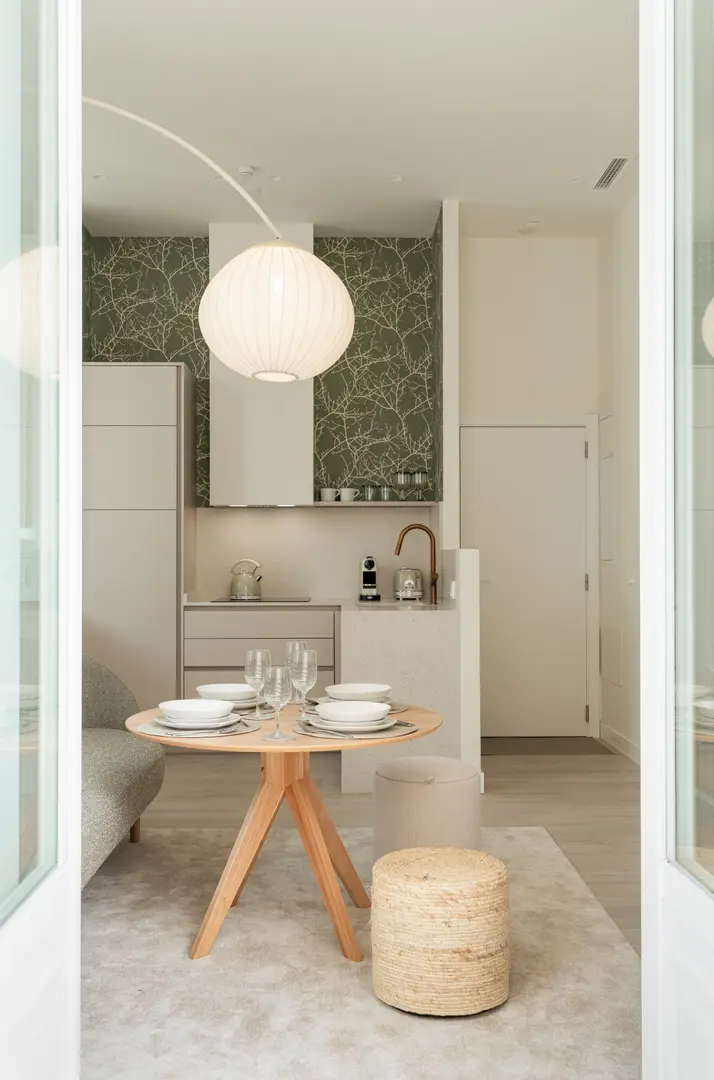 A round wooden dining table set for four under a large spherical lamp in the Oliva residence's open-plan living area