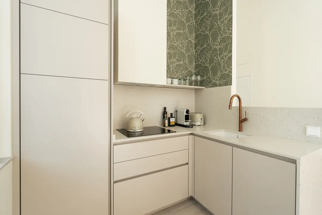 The kitchen in the Oliva residence has light grey handleless cabinets, a stone worktop, induction hob and copper tap, with olive-green wallpaper