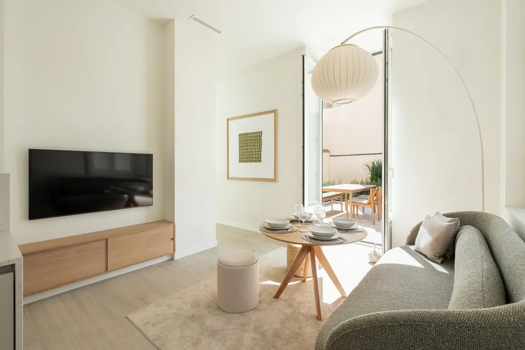 The bright living room of the Oliva residence, with a grey sofa, dining table, and view to a private terrace