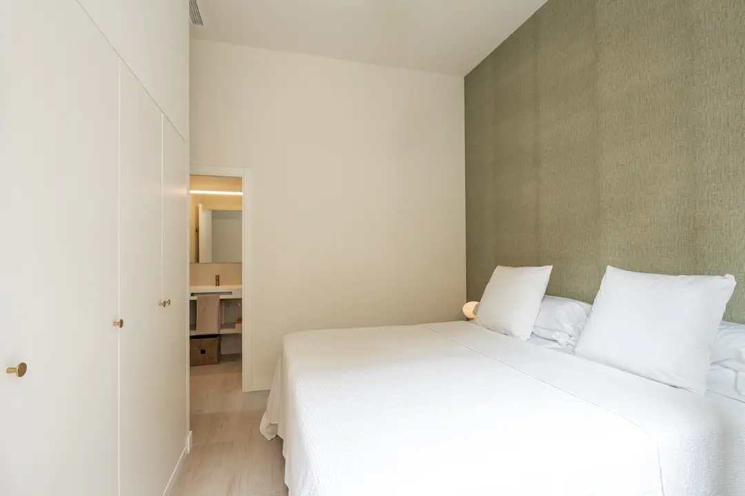 Bedroom in the Oliva residence showing the double bed, white wardrobes, and an open door to the en-suite bathroom