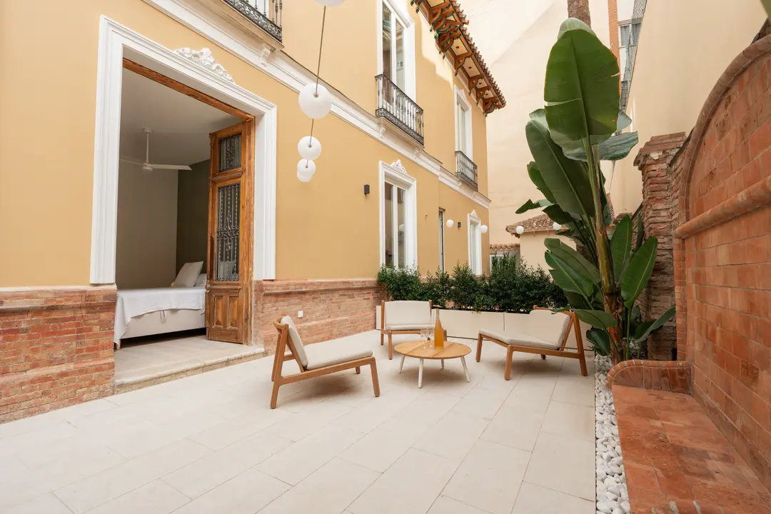The private patio of the Oliva residence, with modern wooden seating and an open doorway showing a bedroom inside