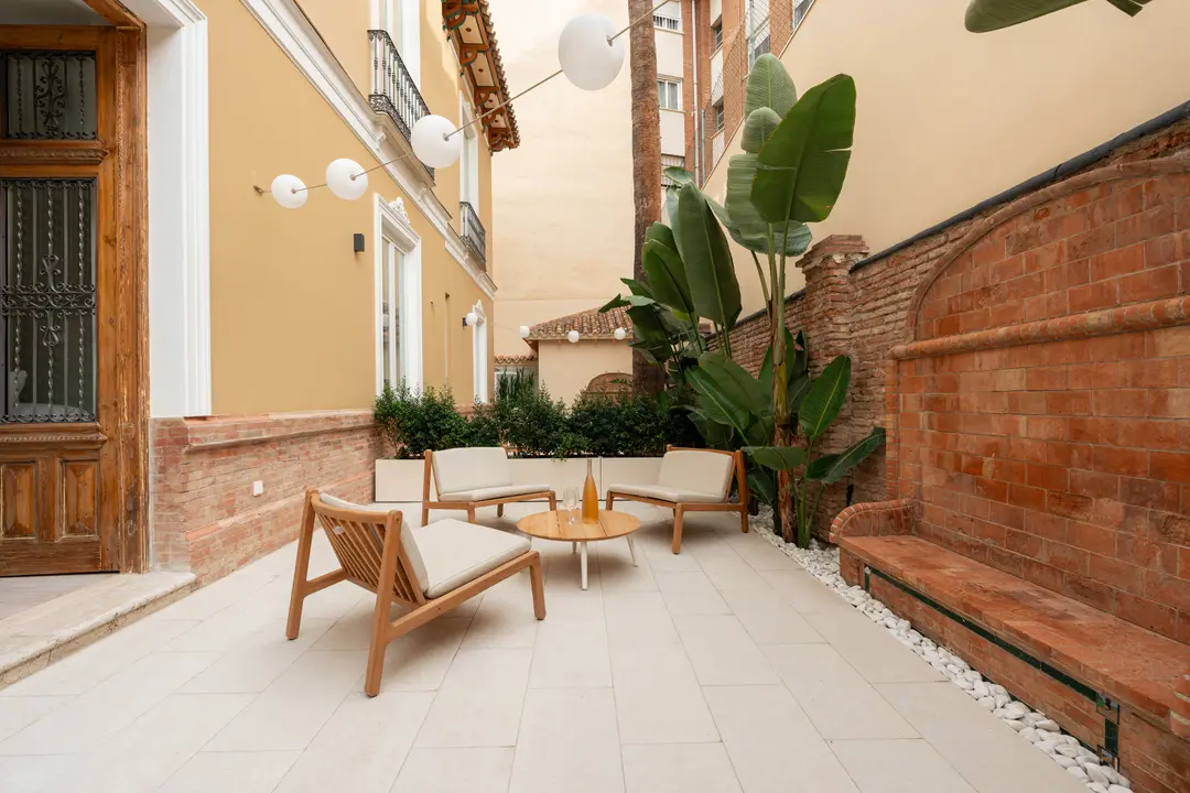 The private terrace of the Oliva residence, with wooden armchairs and a coffee table by a historic brick wall feature