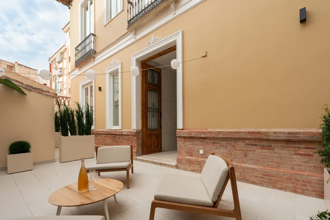 The private terrace of the Oliva residence, with modern wooden armchairs and a coffee table facing the building's ochre facade