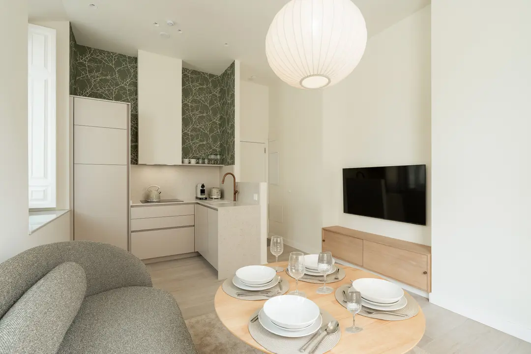 Bright open-plan living area in the Oliva residence, showing the kitchen with green wallpaper, a round dining table, and a sofa