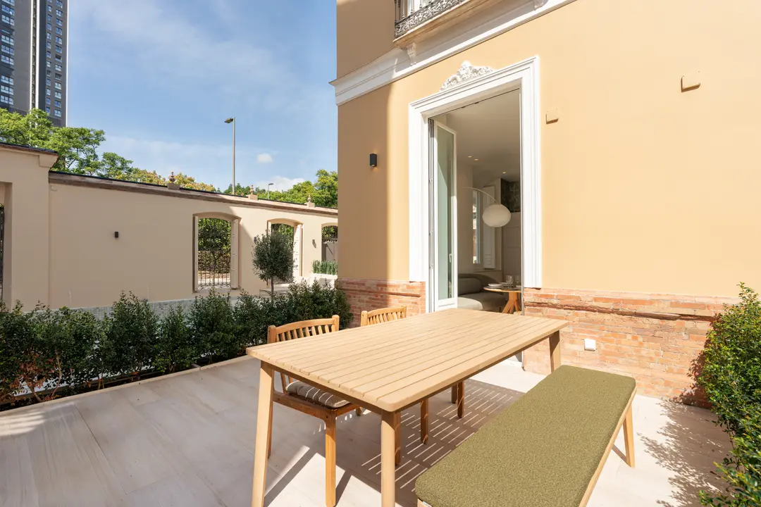 A wooden dining table and green bench on the sunny private terrace of the Oliva residence, looking towards the living room