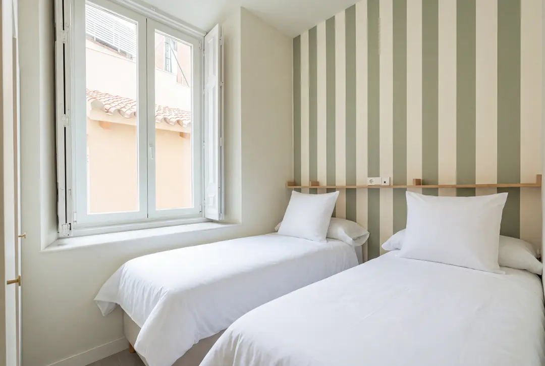 Twin bedroom in the Oliva residence with two single beds, white bedding, and a sage green and white striped feature wall