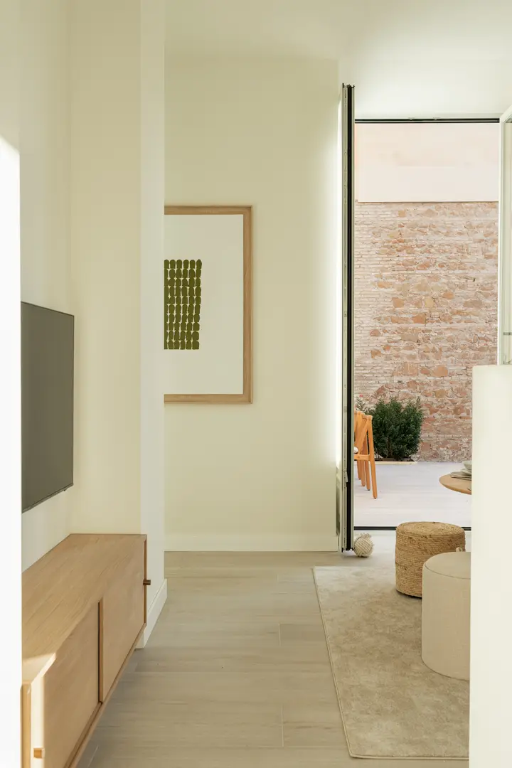 View from the living room of the Oliva residence, with a wooden media unit and framed art, opening onto a private terrace