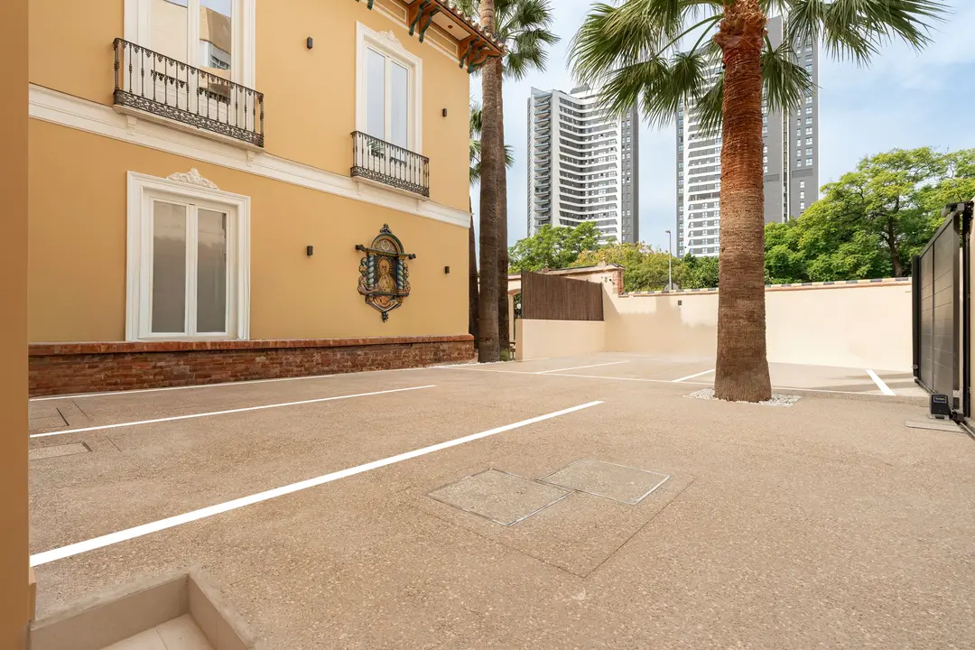 The private parking courtyard at Palacete 10, with marked bays, palm trees, and the historic villa's ochre facade