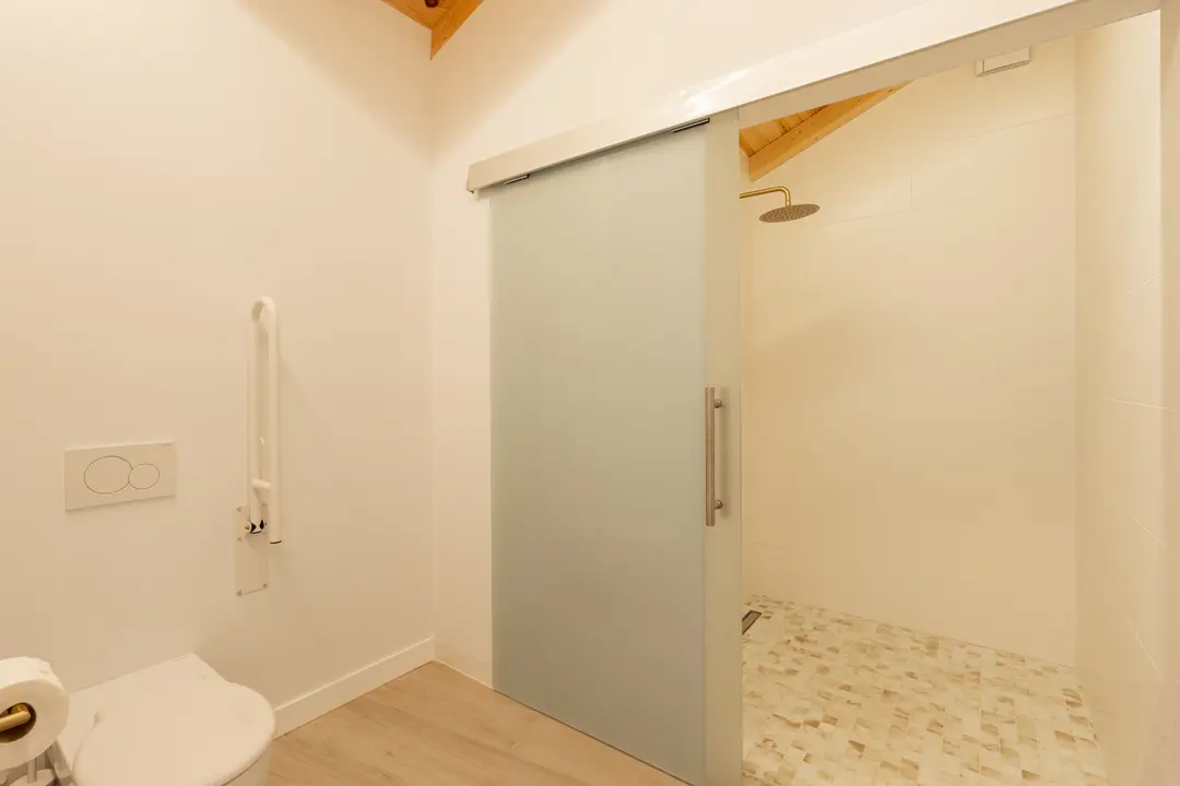 Accessible bathroom in the Toro residence with a toilet, grab rail, and a walk-in shower with a rain head