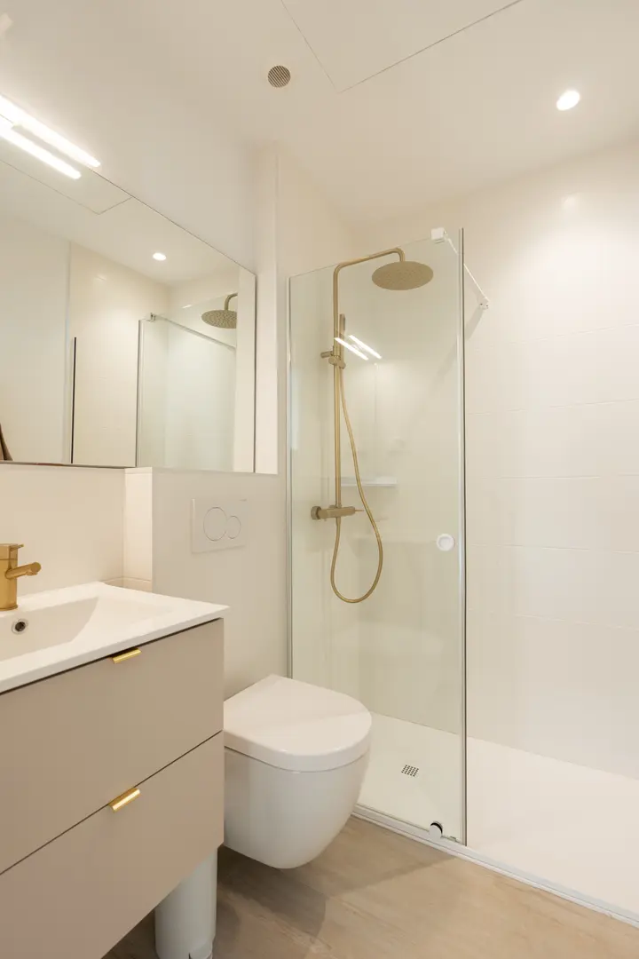 The bathroom in the Toro residence, with a walk-in rain shower, wall-hung toilet, and a beige vanity with gold fittings