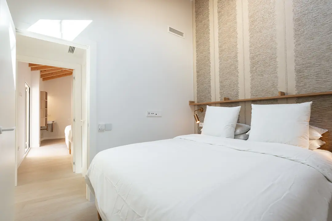 Bedroom in the Toro residence with a double bed, textured wallpaper, and a skylight over the door to the ensuite bathroom