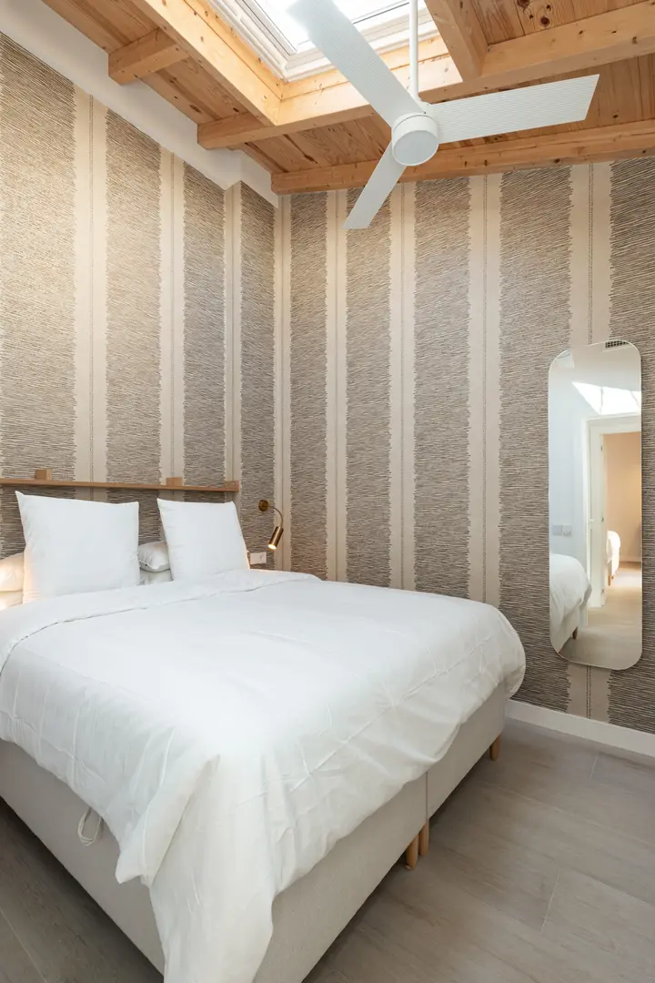 Bedroom in the Toro residence with a double bed, striped wallpaper, and exposed wooden beams under a skylight