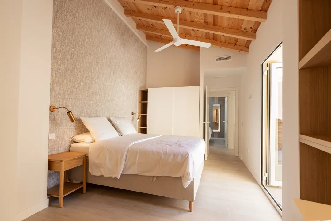 Bedroom in the Toro residence with a vaulted wooden ceiling, a double bed against a textured wall, and light from a terrace door