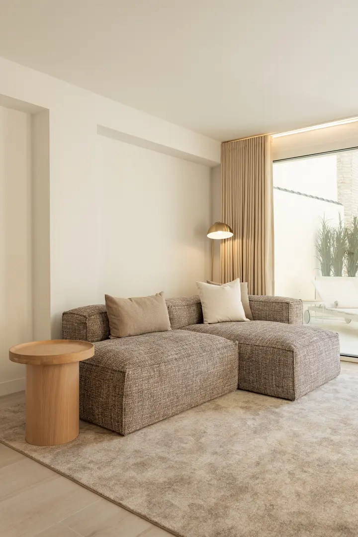 A brown textured chaise sofa and oak side table on a soft rug in the bright living room of the Toro residence