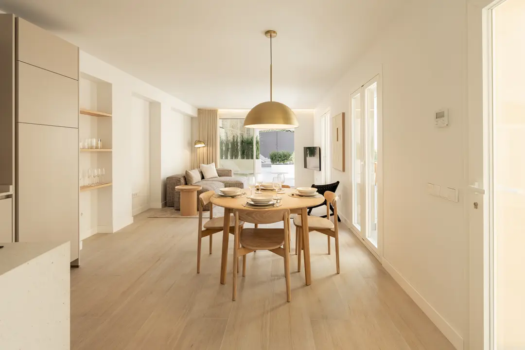 The open-plan dining and living area of the Toro residence, with a round wooden table under a large brass pendant light