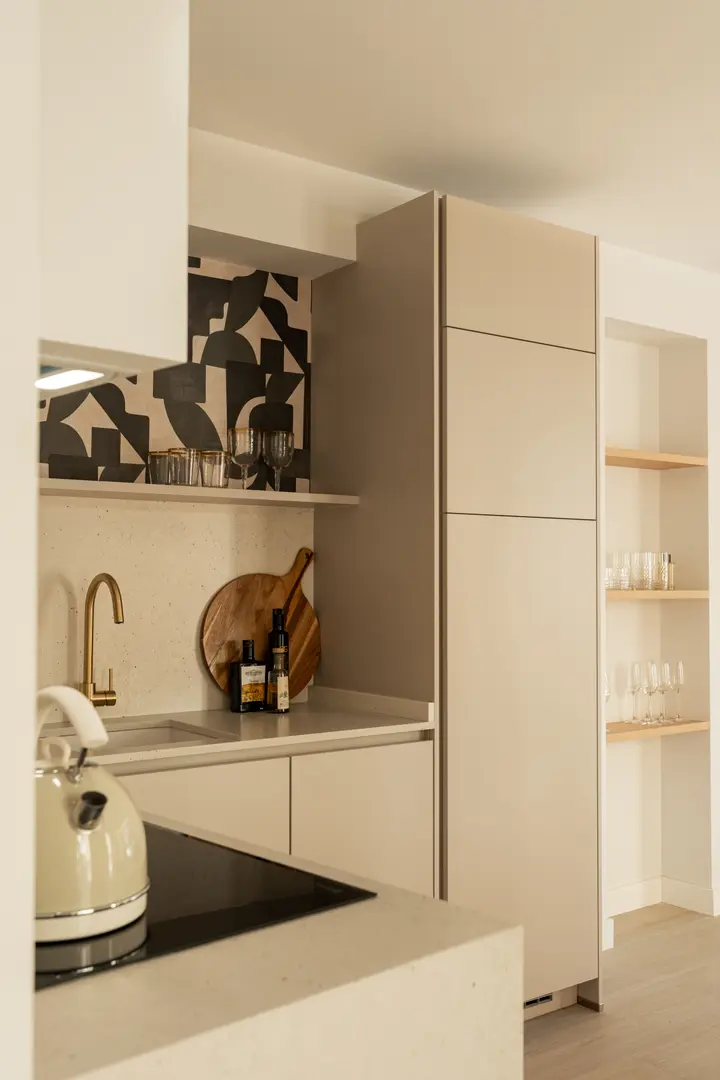 The modern kitchen in the Toro residence features beige cabinets, a brass tap, and a black and white decorative panel