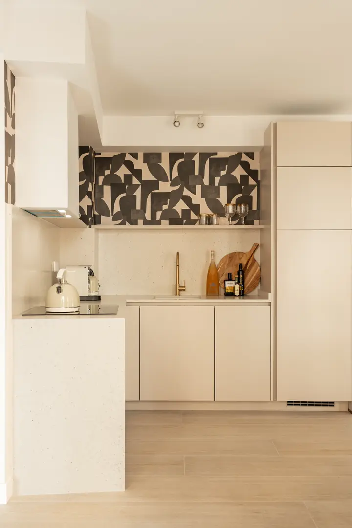 The kitchen in the Toro residence has cream cabinets, a stone worktop, and a bold black and white patterned splashback
