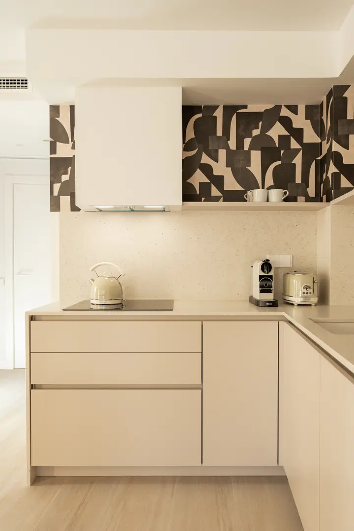 The kitchen in the Toro residence has cream handleless cabinets, a light stone worktop, and striking black and beige wallpaper