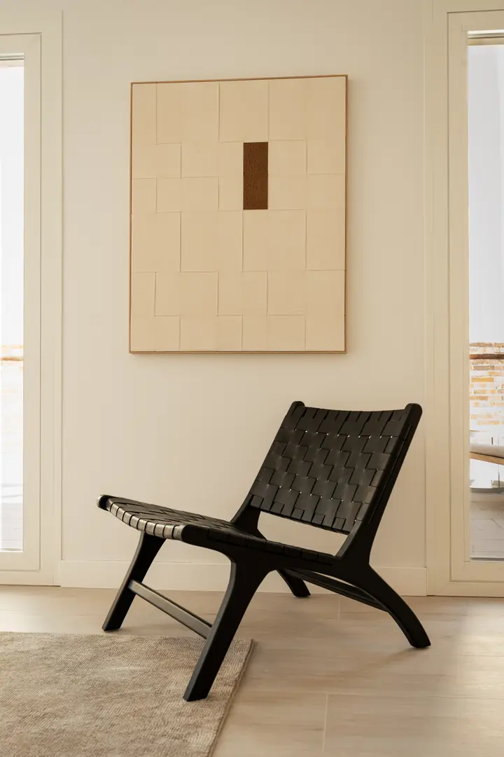 A black woven leather lounge chair in the Toro residence, sitting on a light wood-effect floor below abstract artwork