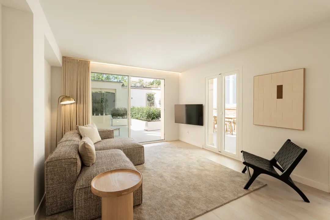 Bright living room in the Toro residence, with a textured L-shaped sofa and a black woven leather chair. Large glass doors open onto a private terrace with planters