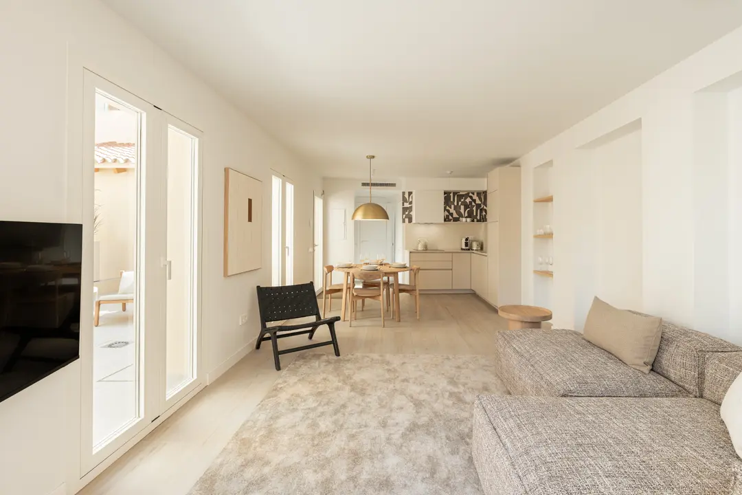 The open-plan living area of the Toro residence, with a sofa, a dining set, and a modern kitchen. French doors open onto a private terrace