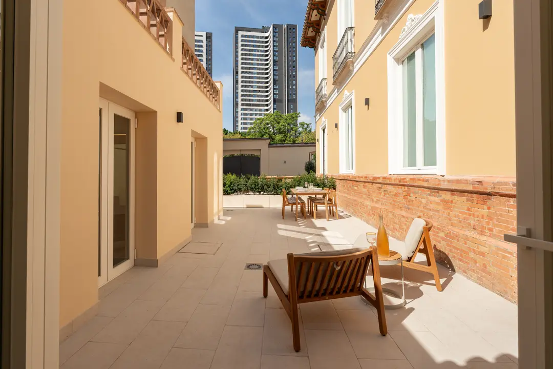 The sunny private terrace of the Toro residence, furnished with a wooden sun lounger and dining set, with modern towers visible