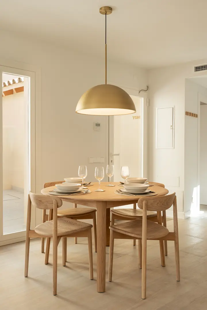 A round oak dining table set for four in the Toro residence, lit by a large brass dome pendant light