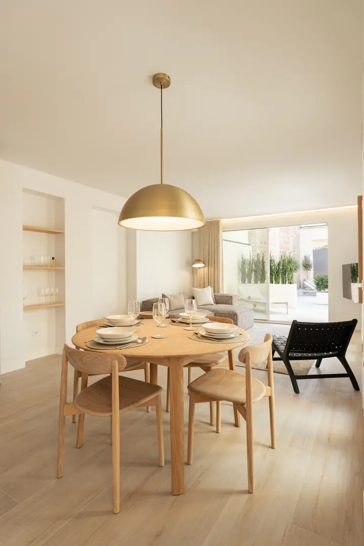 A round wooden dining table set for four in the Toro residence, with the living area and private terrace beyond